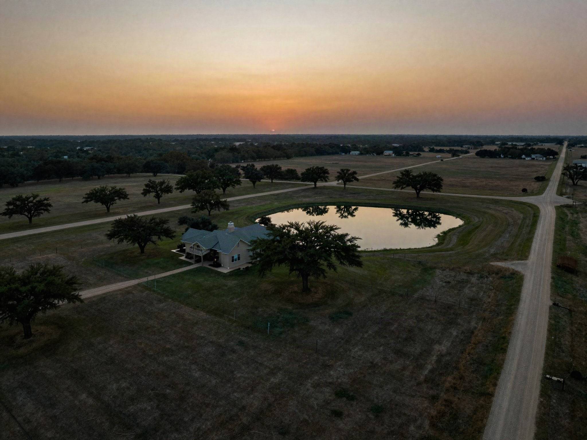 Ranch land with a stock pond and oak trees at dusk